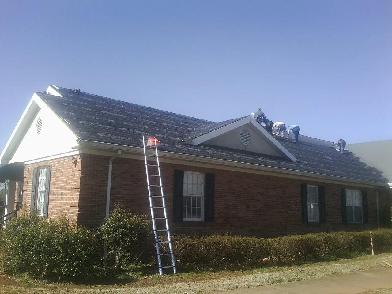 Crew tearing shingles off a brick ranch roof with a ladder set — Metal Roof Repair work by our crew in Tehama