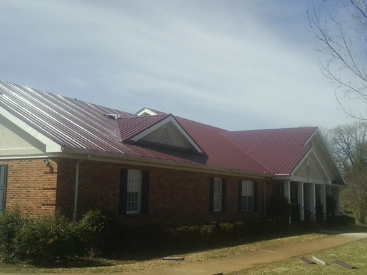 Red metal roof with gabled entries on a long brick building, from a Hail Damage Roof Repair job in Tehama