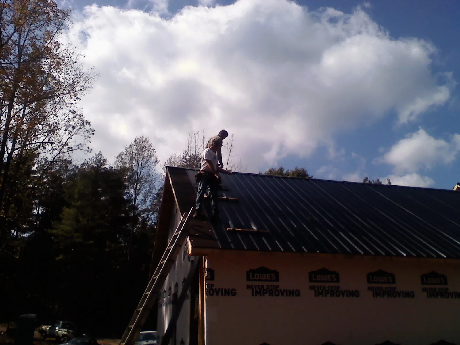 Roofer fastening dark metal panels high against a cloudy sky, from a Roof Inspection job in Tehama