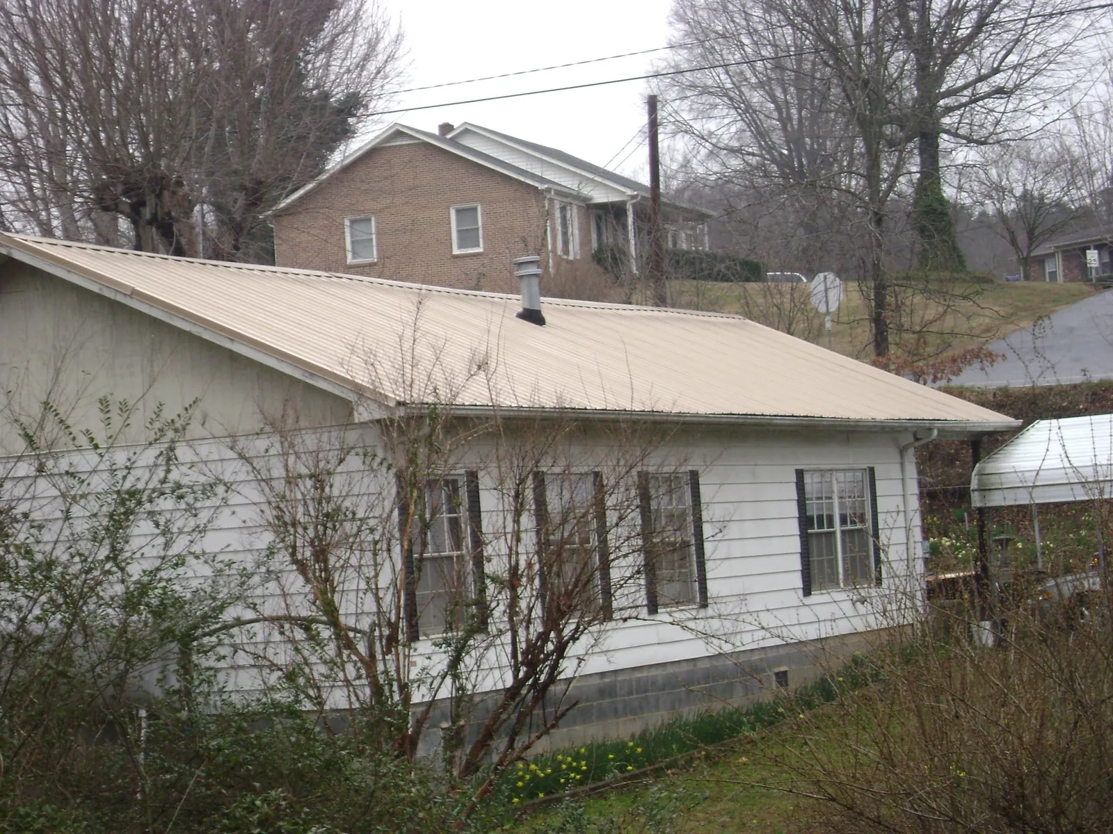 Tan metal roof on a white sided house set into a hillside — Commercial Roofing by Roofing Brothers in Tehama